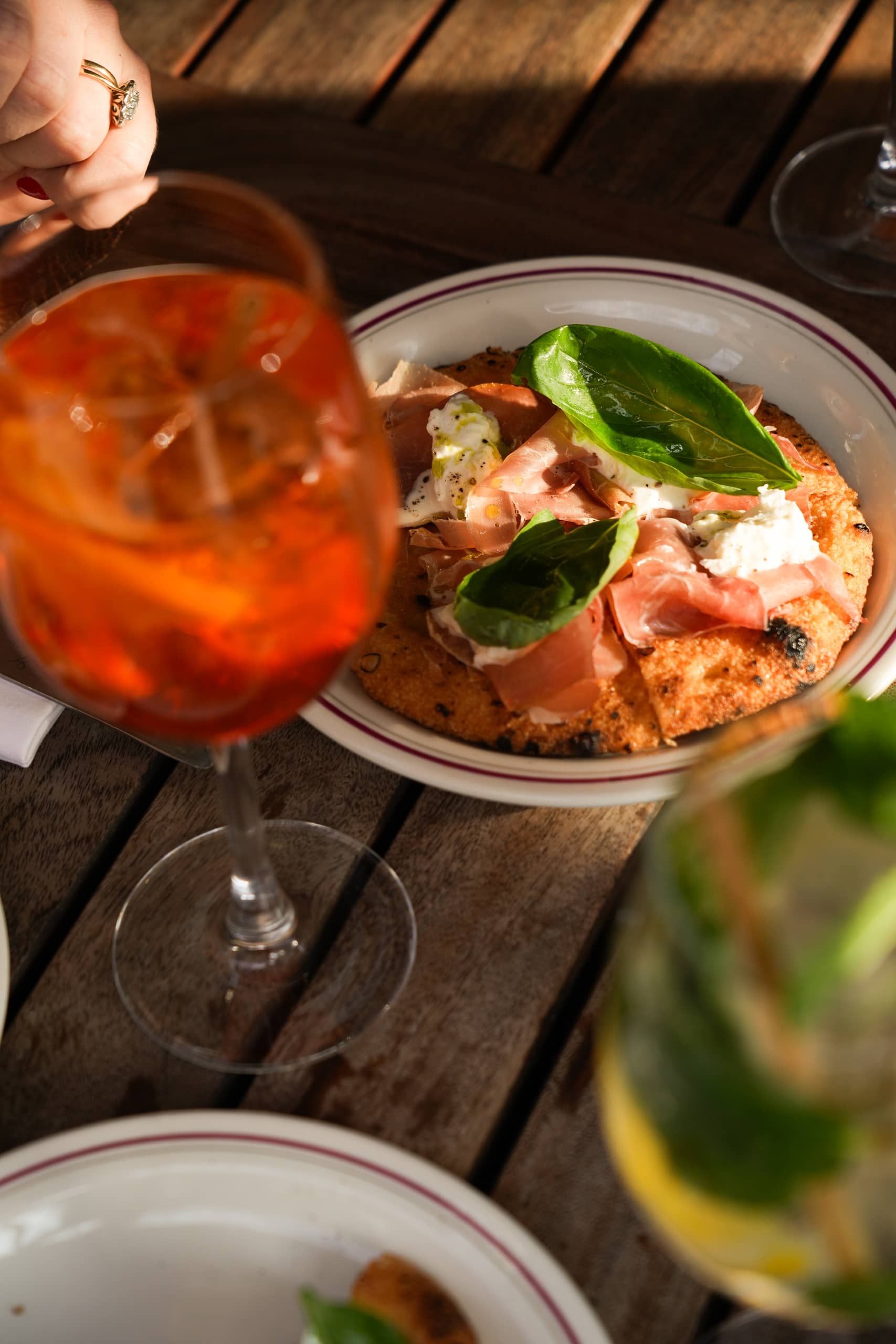 Focaccia topped with prosciutto, burrata, and fresh basil leaves served with an Aperol spritz at Mortimer House Kitchen