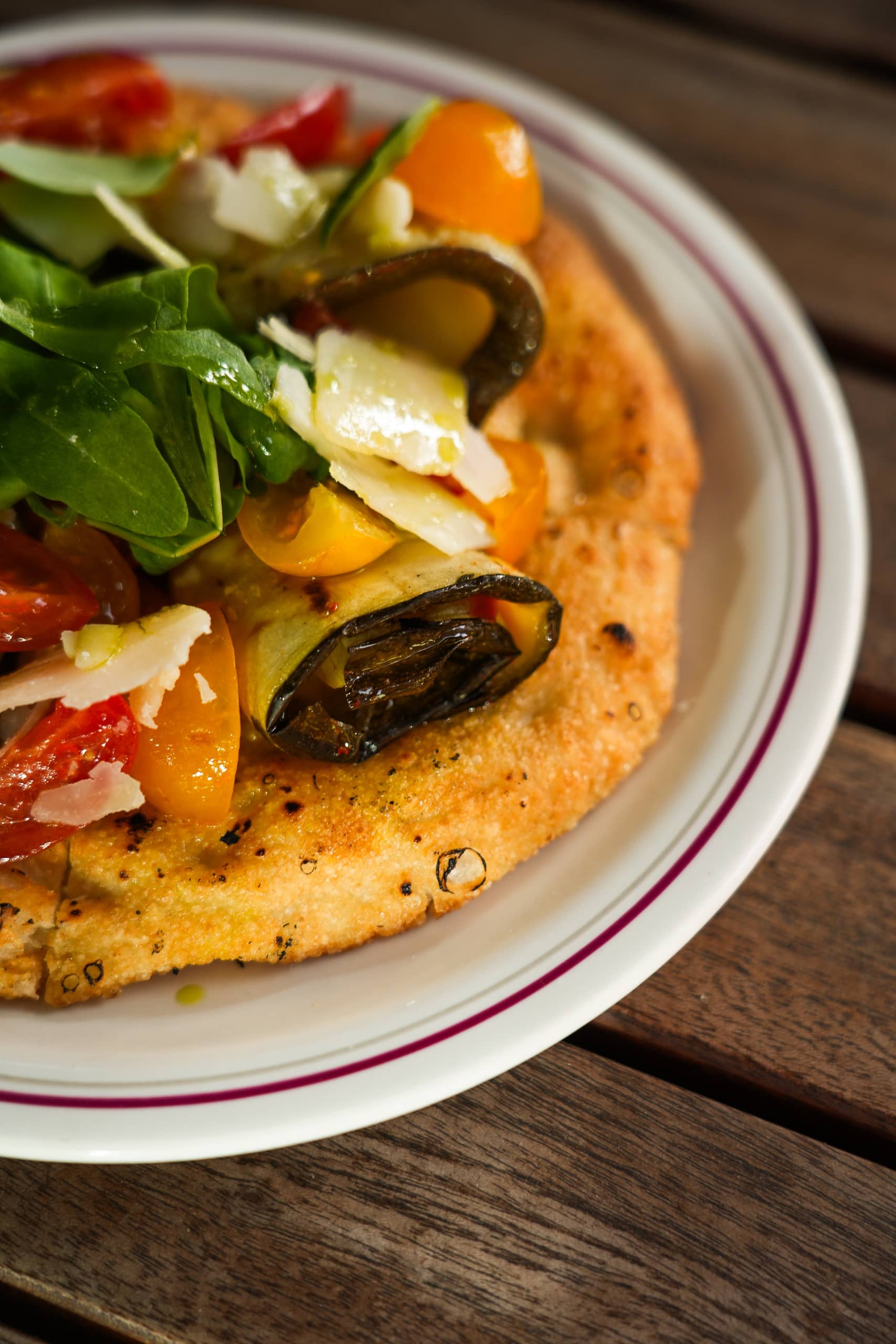 Focaccia topped with roasted courgette, cherry tomatoes, arugula, and parmesan shavings at Mortimer House Kitchen
