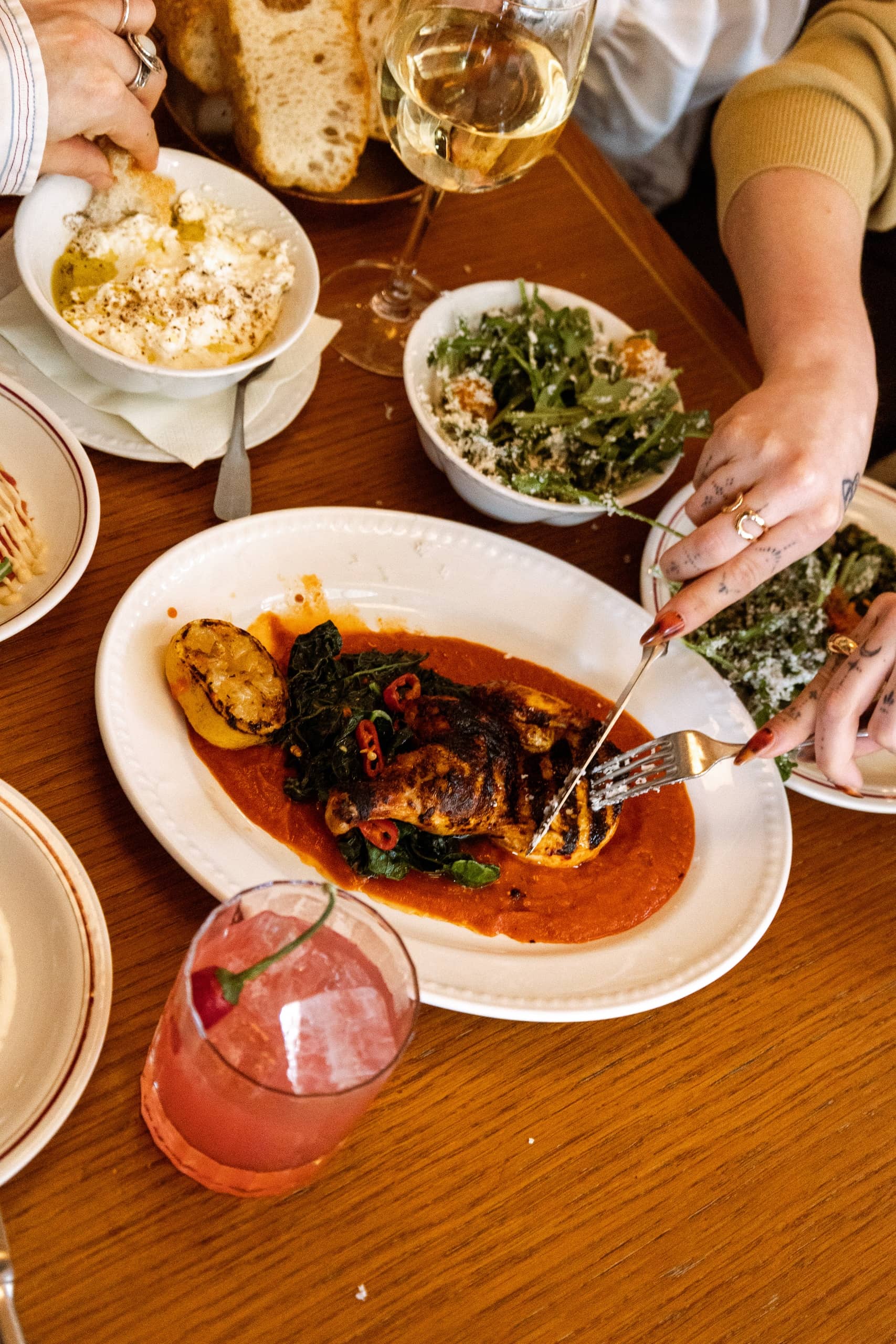Grilled chicken with wilted greens, charred lemon, and red pepper in tomato sauce, served with fresh bread, burrata, salad, and wine at Mortimer House Kitchen.
