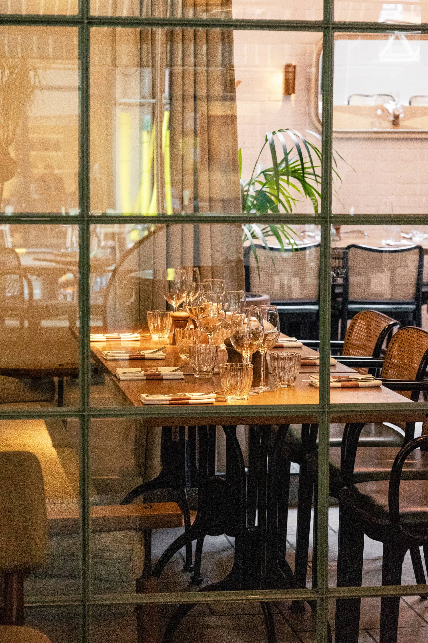 Elegant dining table set with wine glasses, water glasses, and cutlery inside Mortimer House Kitchen, viewed through window panes
